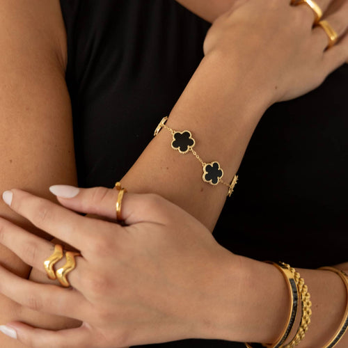 Close-up of hands wearing gold jewelry with black clover accents.